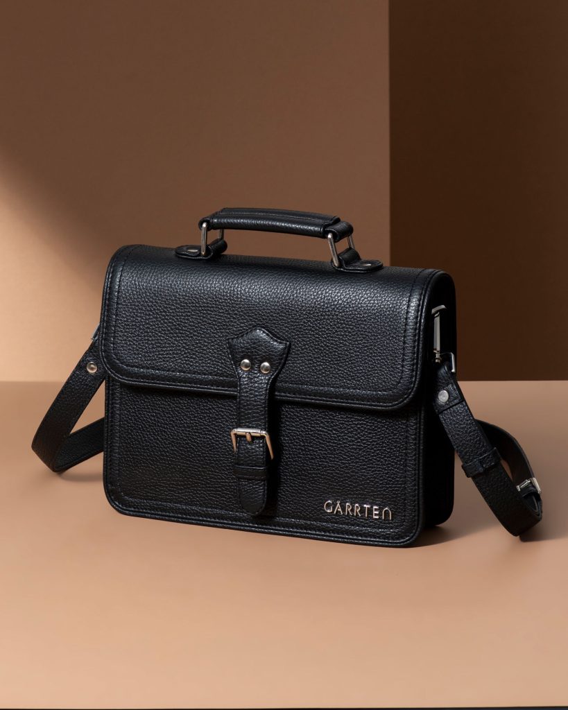 Black leather satchel bag with buckle strap and shoulder sling.