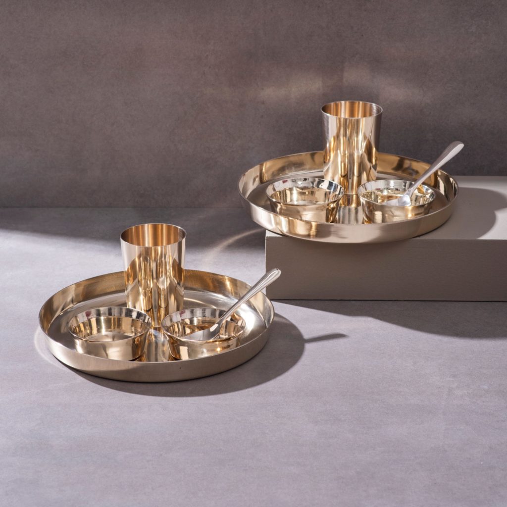Brass thali dinnerware sets with plates bowls glasses and spoons on textured surface