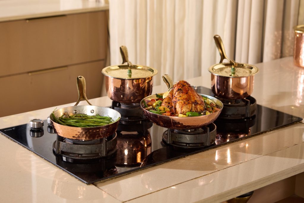 Copper cooking pans and pots on gas stove with roasted chicken and vegetables