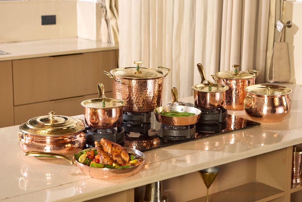 Copper cookware collection on kitchen counter with food and gas stove setup