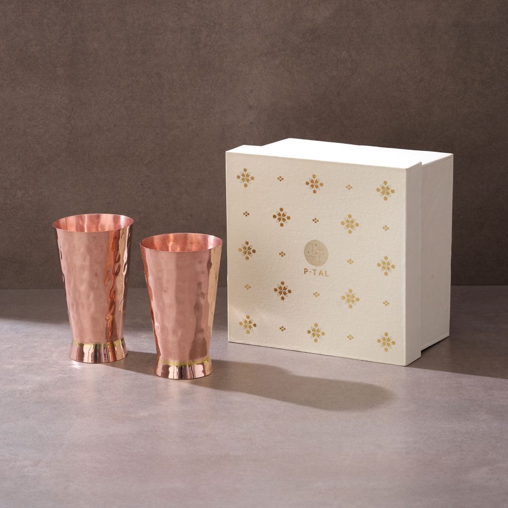 Two copper tumblers displayed with cream premium gift box on textured background