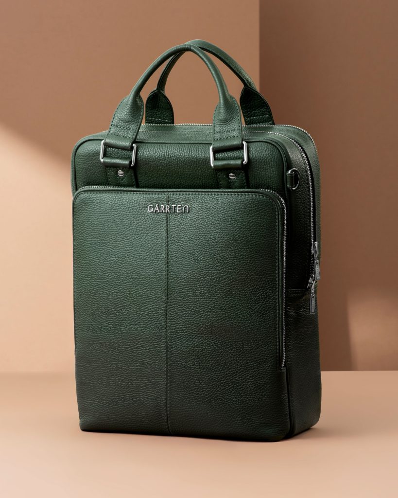 Green leather briefcase laptop bag with top handles on beige studio background.