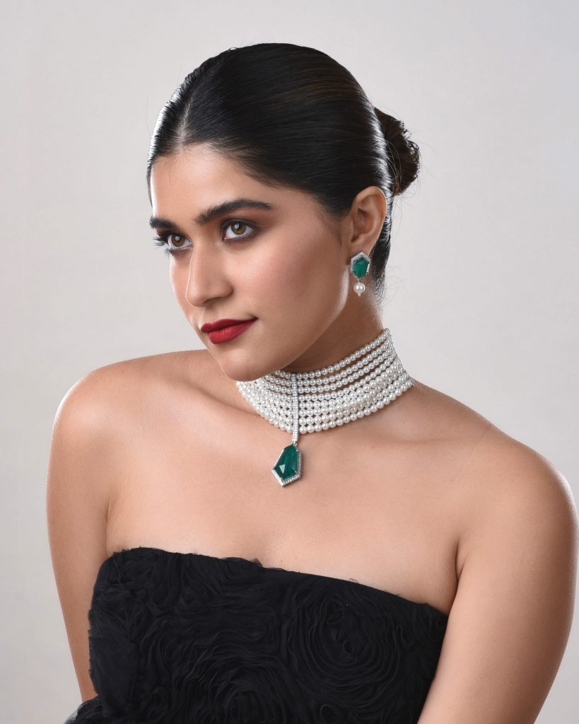 Model wearing pearl choker with green pendant and matching green earrings.