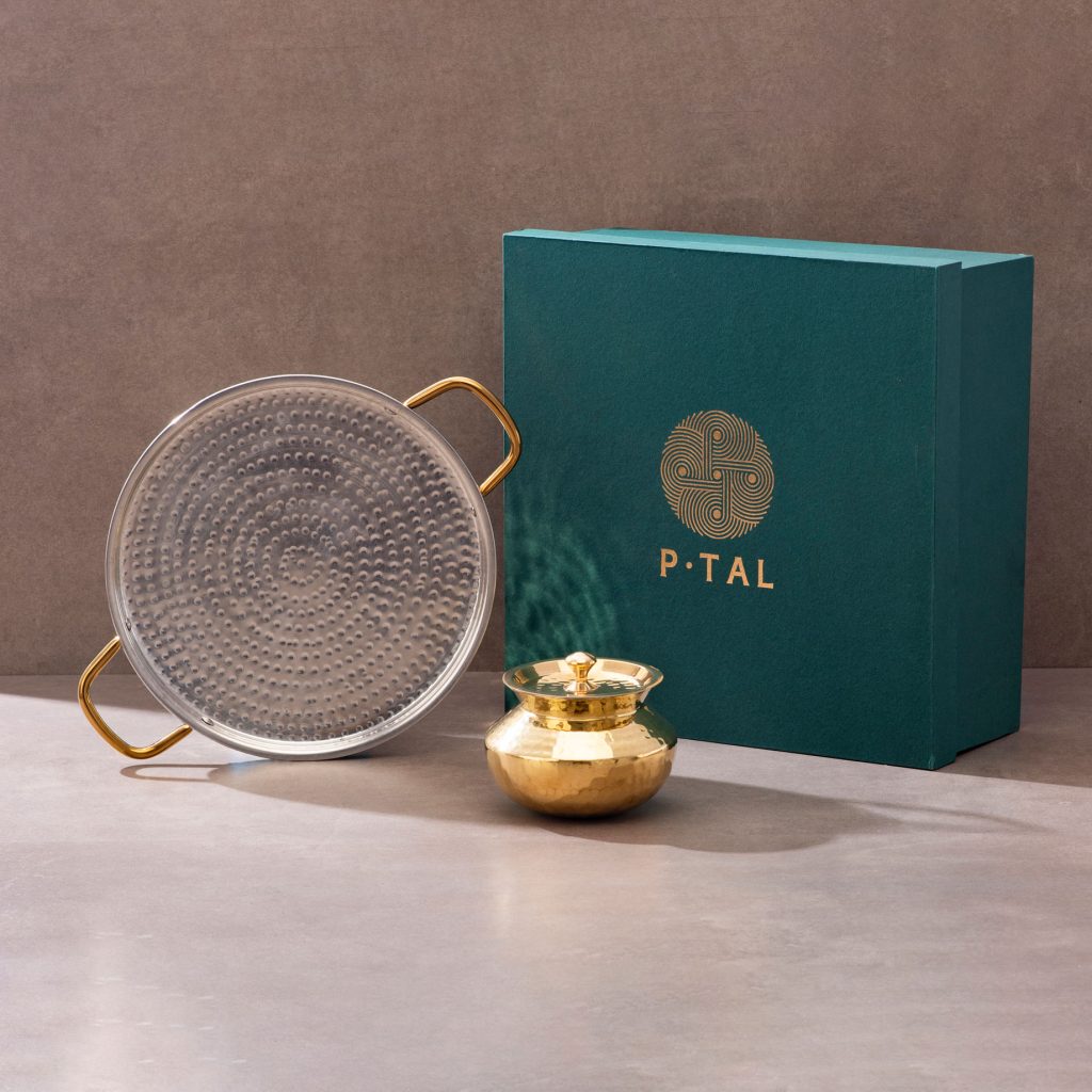 Hammered brass kadhai with long polished handle against textured studio background