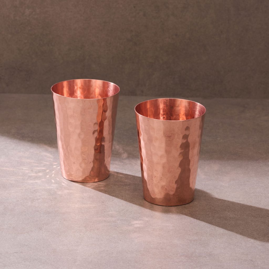 Two hammered copper tumblers on textured studio background