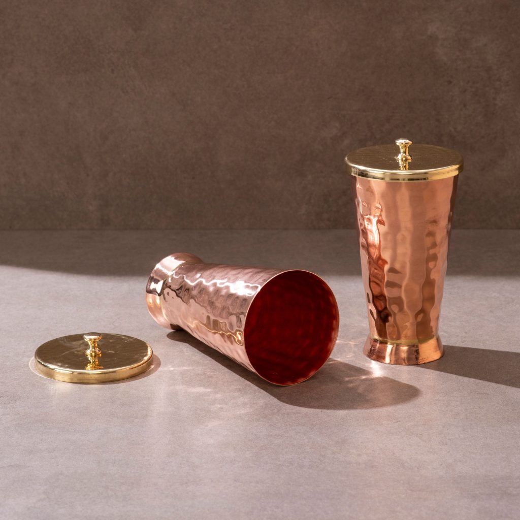 Lidded copper tumblers with brass covers on textured studio surface