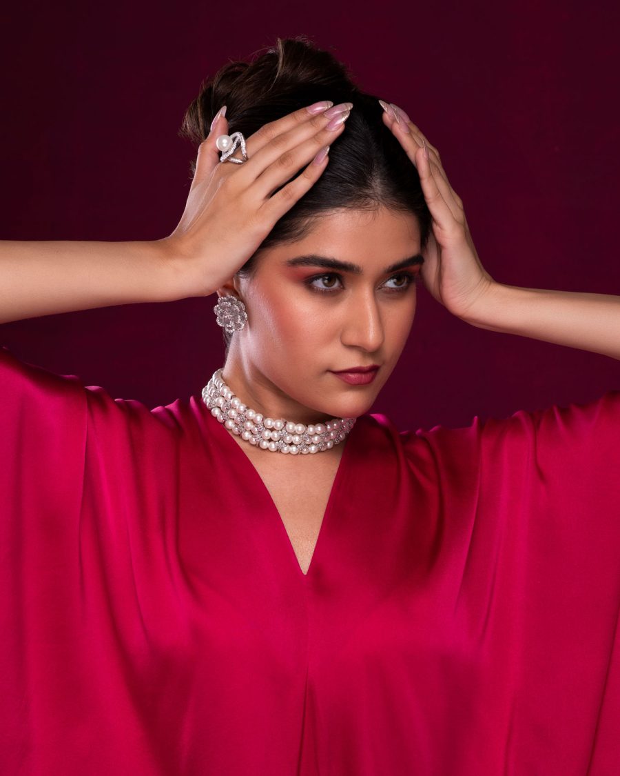 Model wearing pearl choker, statement ring, and earrings with magenta outfit.
